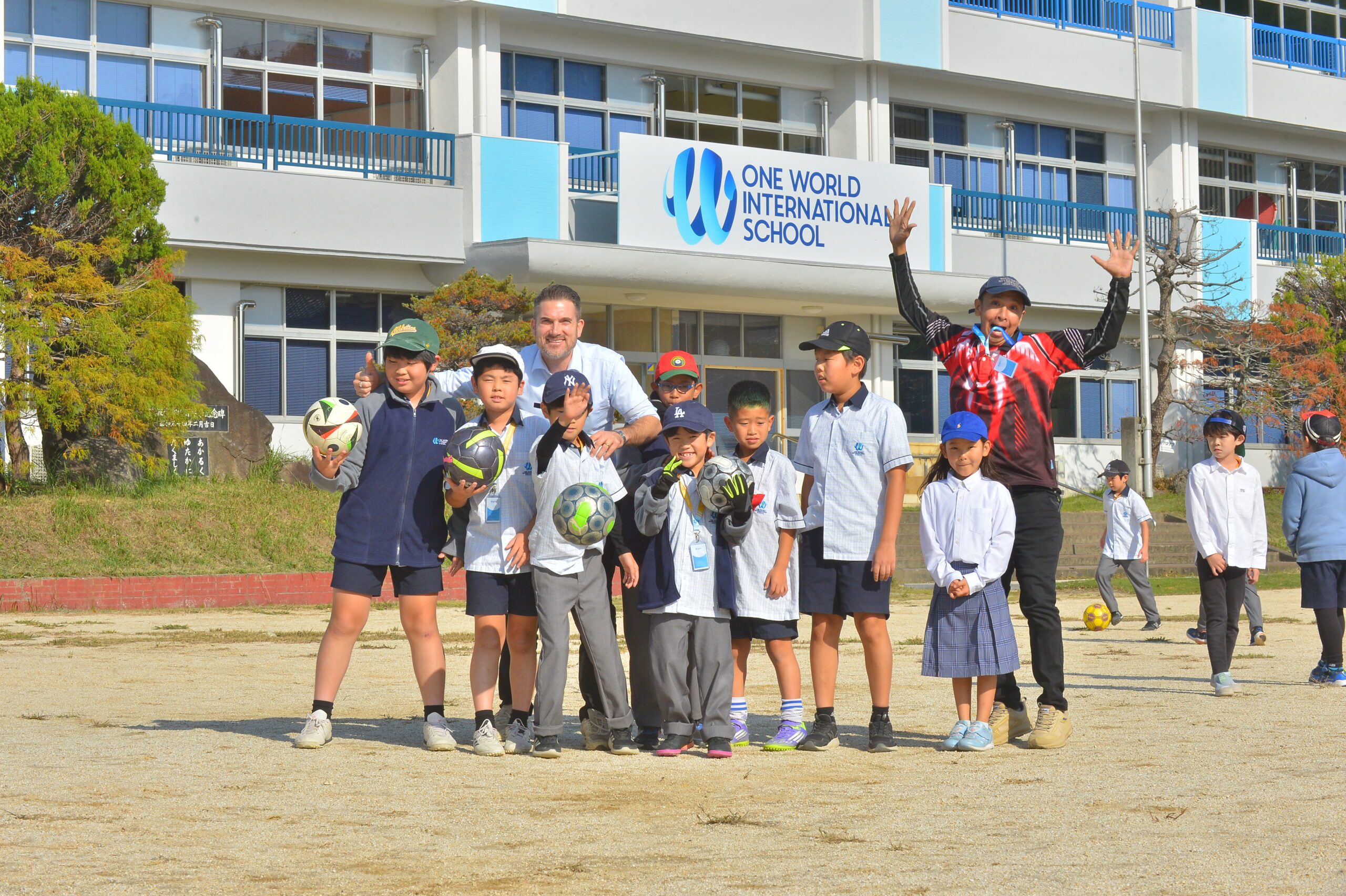 Teachers at OWIS Tsukuba with students on the field, jumping and playig with footballs - kindness