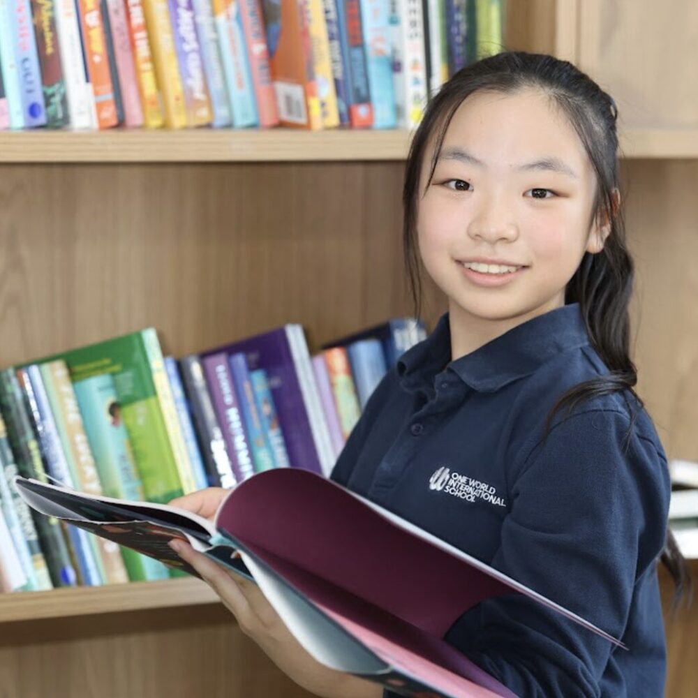 Primary school age Girl student holding book in library at OWIS Osaka